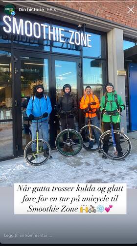 Four men are standing with unicycles standing in front of a sign that reads, "Smoothie Zone". They are warmly wrapped up and there is snow on the ground.