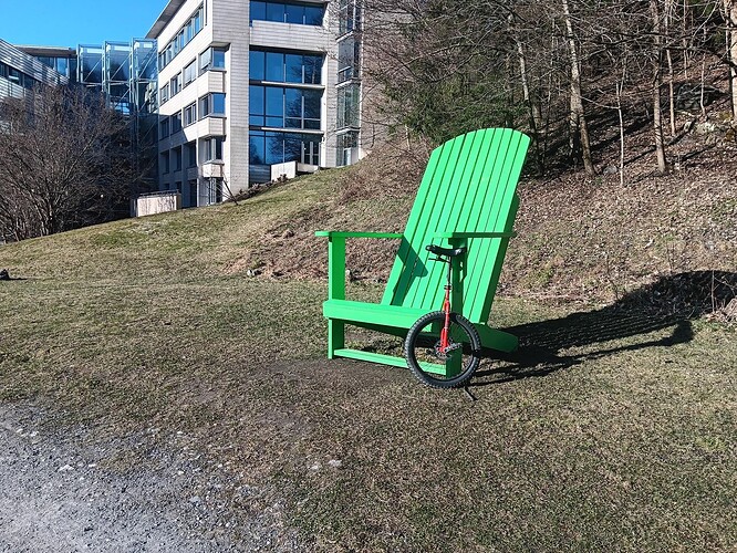 Small unicycle next to a green, lounger style wooden chair