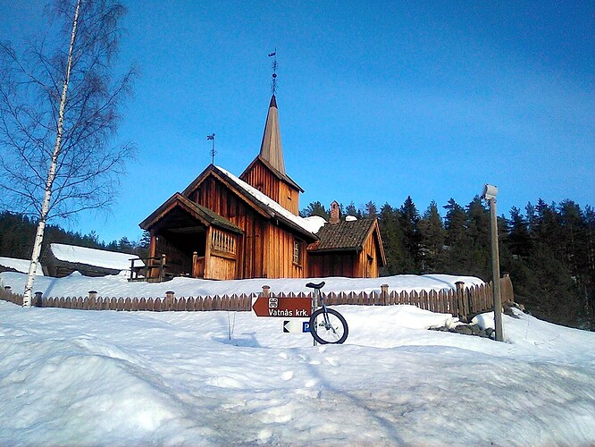 Old wooden church with snow all around, blue skies and a unicycle in the foreground