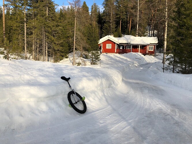 Red cabin in the background with unicycle in foreground. Snow on the ground