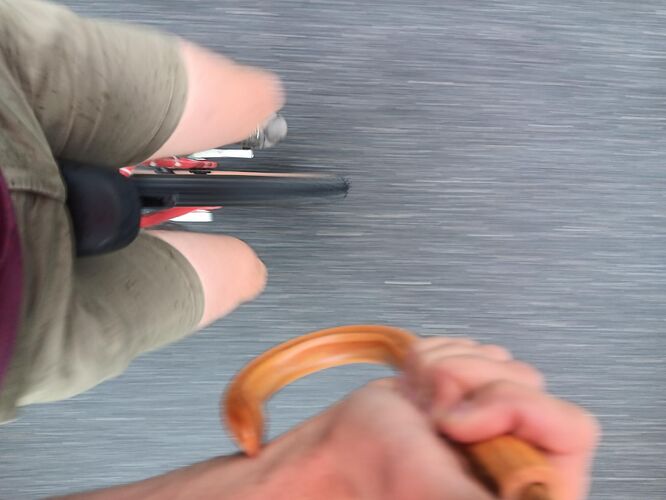 View looking down at a unicycle from the point of view of the rider. You can also see the rider's right hand holding the handle for an umbrella.